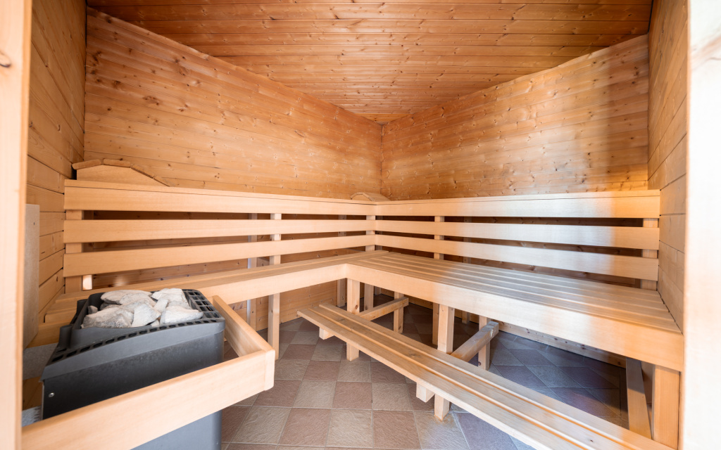 Holzsauna mit hellen Sitzbänken, Saunaofen mit Steinen und gefliestem Boden